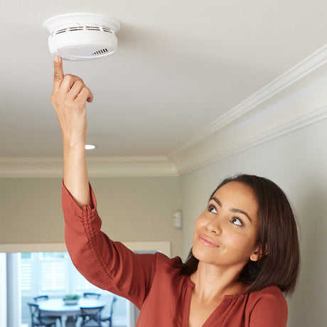 A woman checking a smoke detector in a house