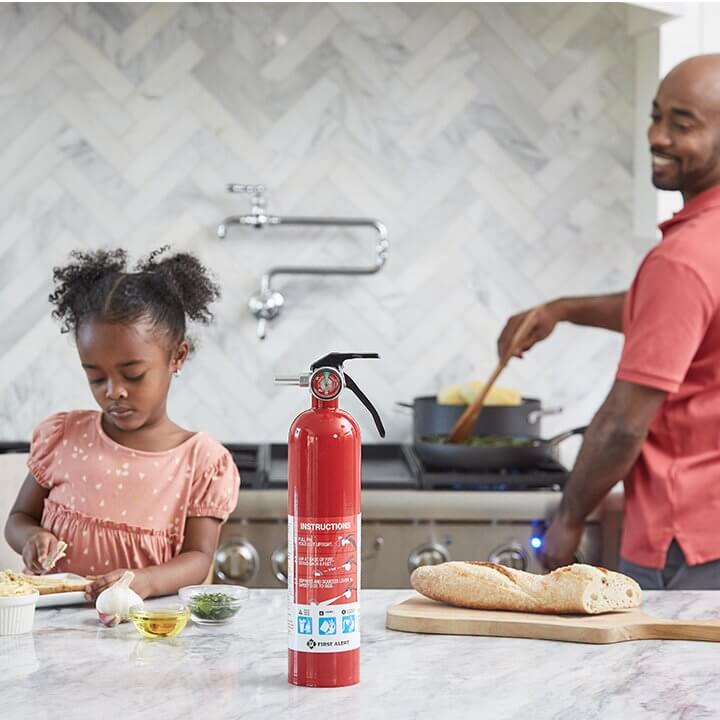 A father and daughter cook a meal in the kitchen. A bottle of EZ Fire Spray is on the counter.
