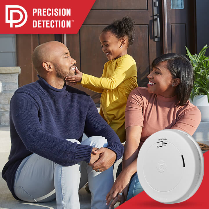Precision Detection. A man and woman sit outside their home with their young daughter. A smoke alarm is shown in the lower right corner. 